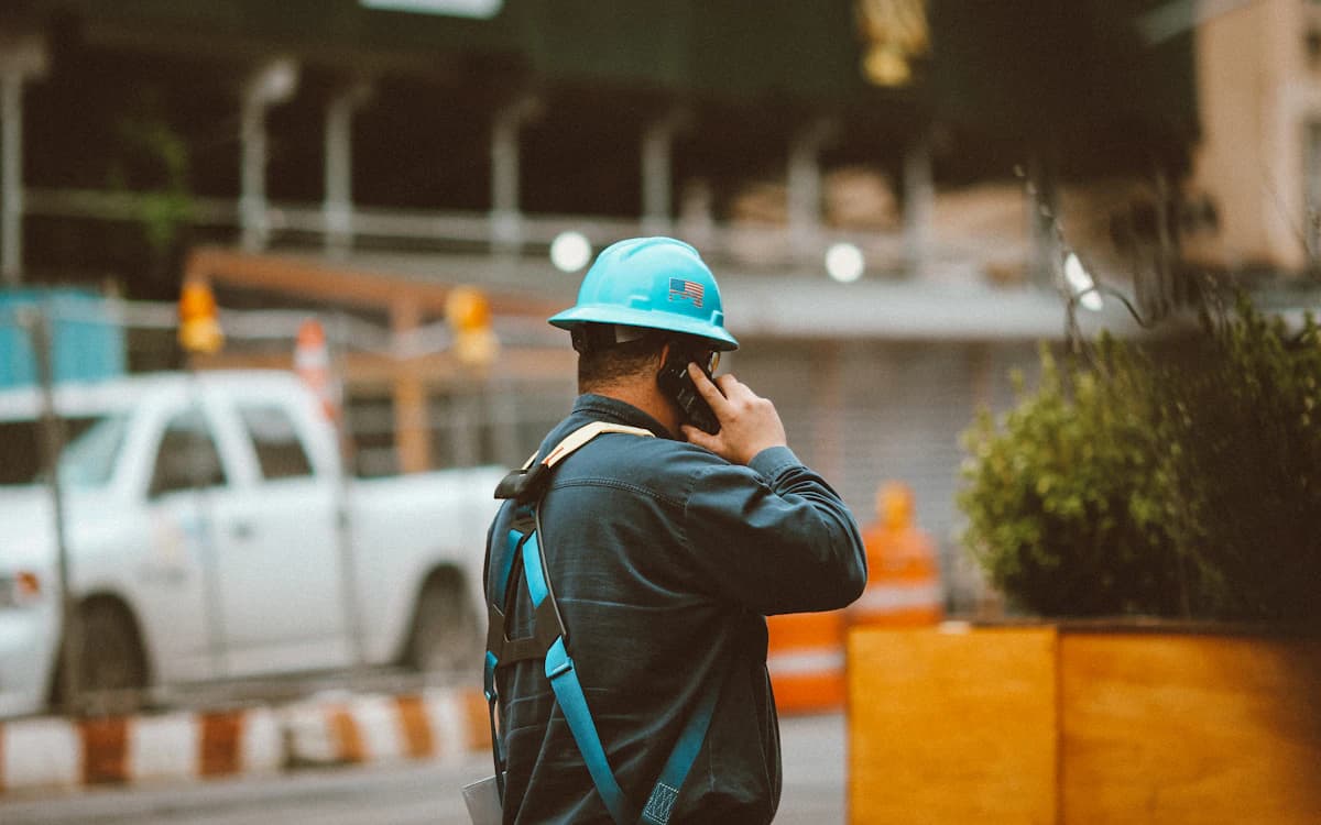 A worker in a hard hat on a phone call beside a pickup truck at a job site