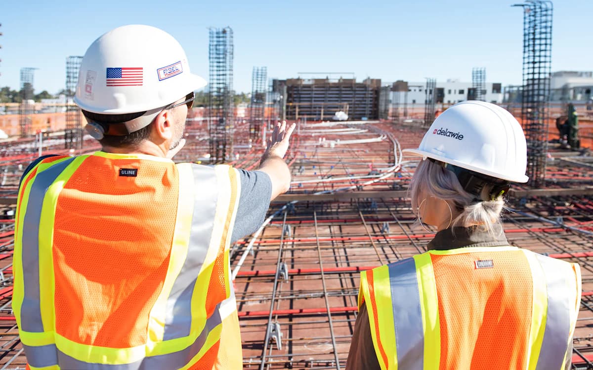 Two workers in high-visibility vests reviewing site plans on a construction site